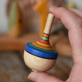 Mader traditional rainbow striped spinning top toy in an adult's hand.