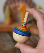 Mader traditional rainbow striped spinning top toy in an adult's hand.