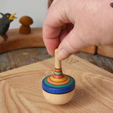 Mader traditional rainbow striped spinning top being placed on an ask spinning plate in the Babipur playroom. 