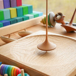 Mader wooden Trumpo spinning top on a Mader spinning plate surrounded by wooden spinning tops and a Grimms Large Stepped Pyramid