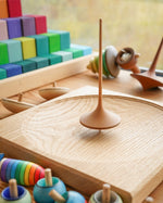 Mader wooden Trumpo spinning top on a Mader spinning plate surrounded by wooden spinning tops and a Grimms Large Stepped Pyramid
