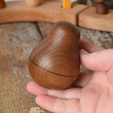 Mader Kreiselmanufaktur walnut roly-poly pear wooden toy being placed on a wooden surface in the Babipur playroom. 