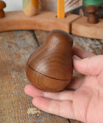 Mader Kreiselmanufaktur walnut roly-poly pear wooden toy being placed on a wooden surface in the Babipur playroom. 