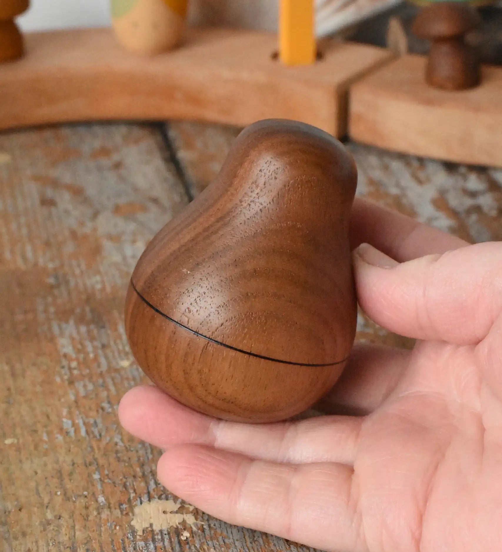 Mader Kreiselmanufaktur walnut roly-poly pear wooden toy being placed on a wooden surface in the Babipur playroom. 