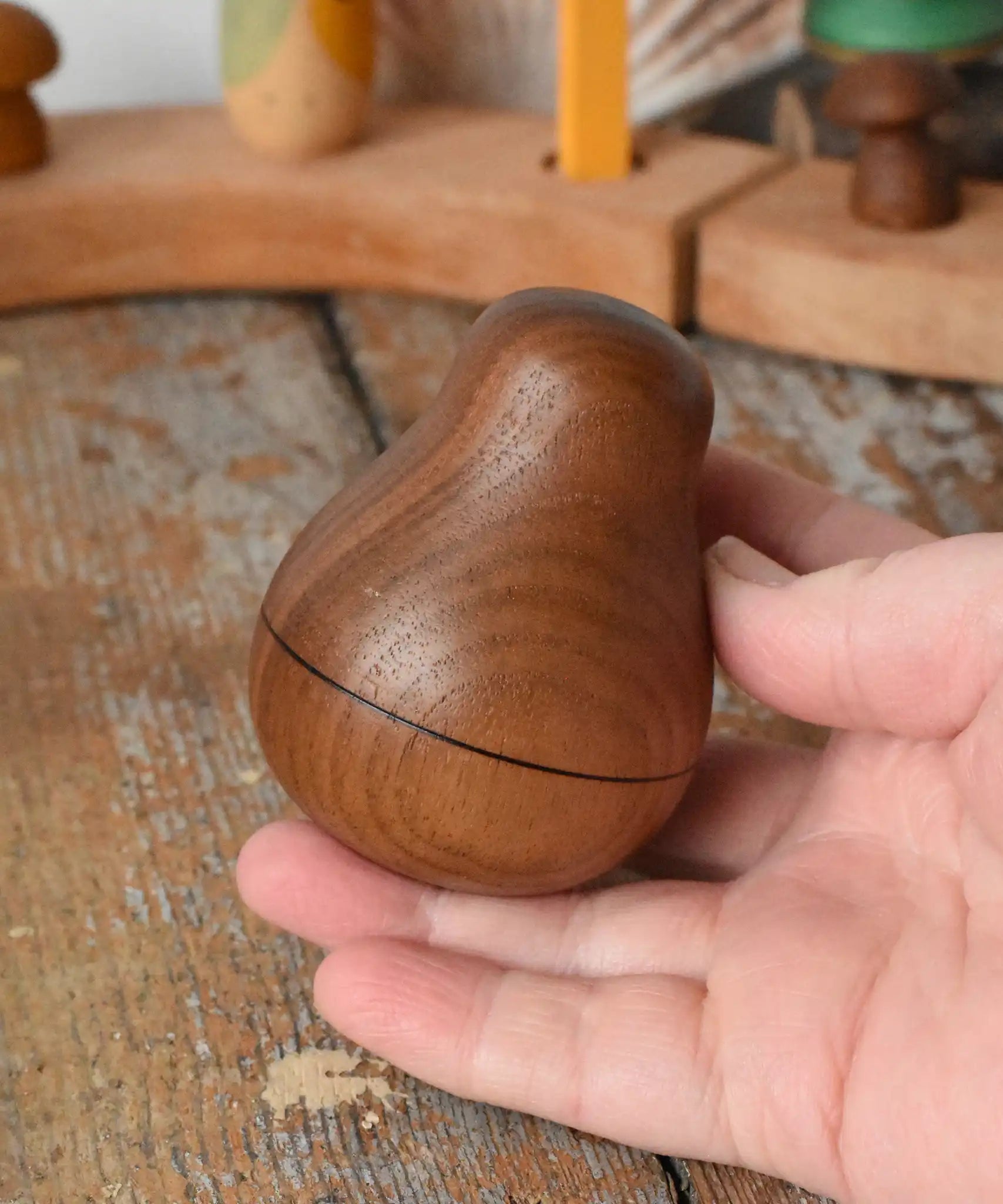 Mader Kreiselmanufaktur walnut roly-poly pear wooden toy being placed on a wooden surface in the Babipur playroom. 