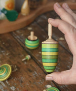 Thunderbolt spinner from the Mader Kreiselmanufaktur green grass spinning top learning set in an adult's hand in the Babipur playroom.