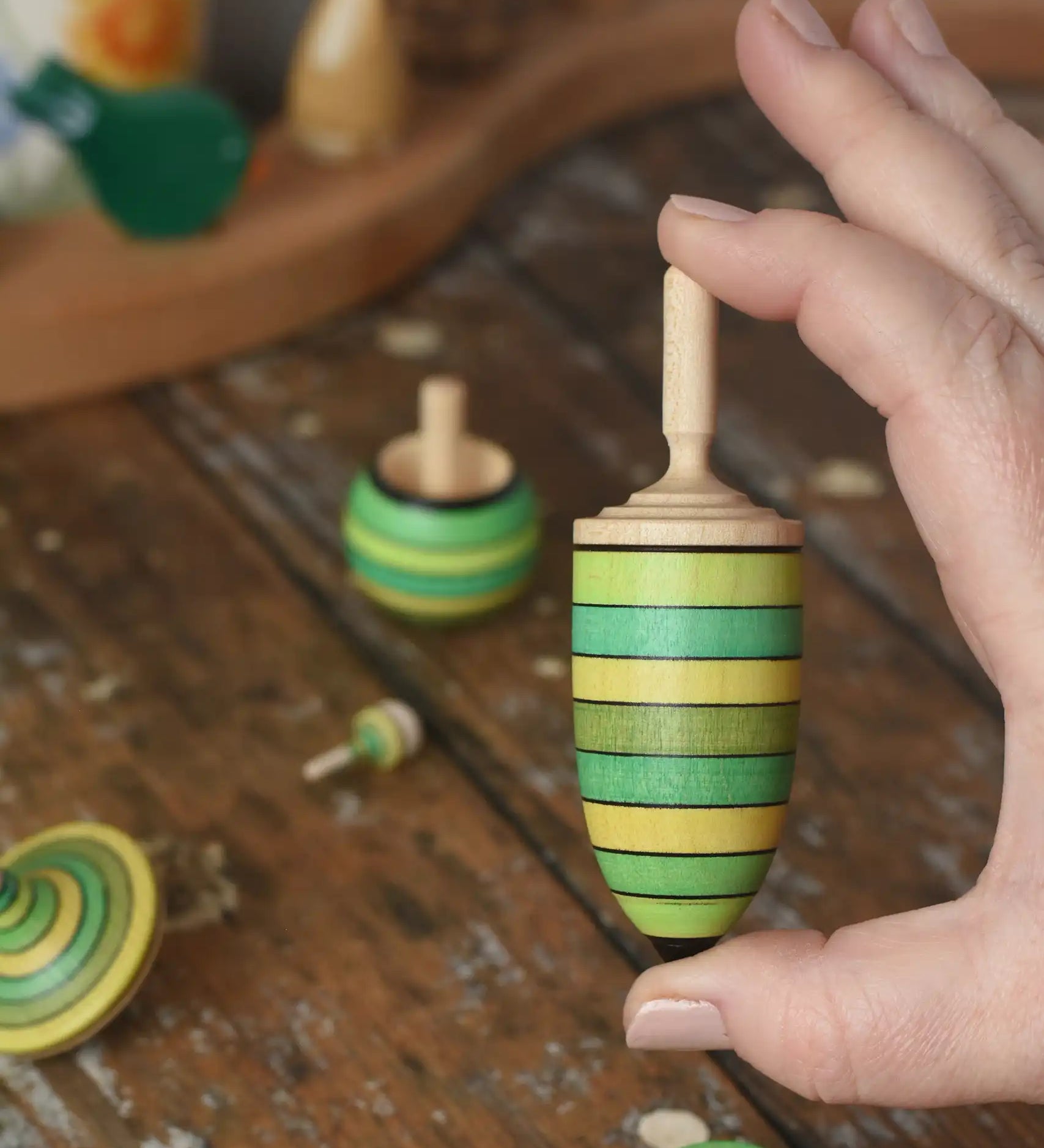 Thunderbolt spinner from the Mader Kreiselmanufaktur green grass spinning top learning set in an adult's hand in the Babipur playroom.