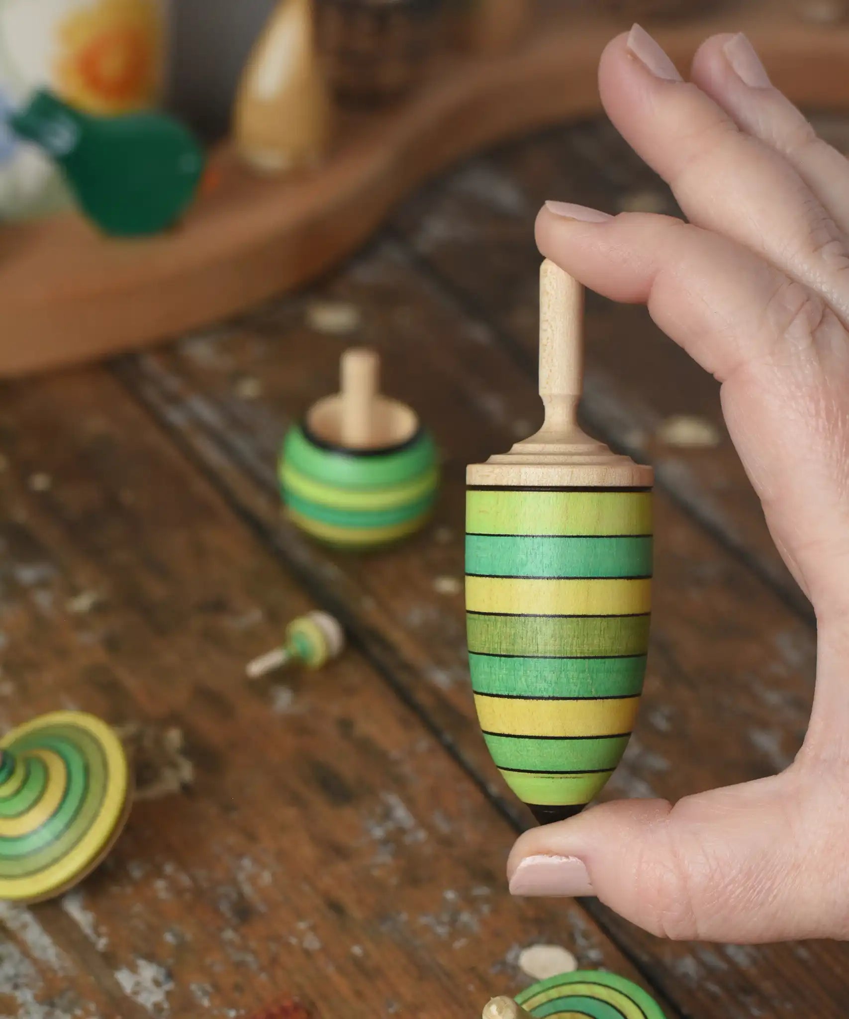 Thunderbolt spinner from the Mader Kreiselmanufaktur green grass spinning top learning set in an adult's hand in the Babipur playroom.