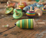 The miniature and thunderbolt spinners from the Mader Kreiselmanufaktur green grass spinning top learning set placed on a wooden surface next to each other in the Babipur playroom. 