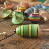 The miniature and thunderbolt spinners from the Mader Kreiselmanufaktur green grass spinning top learning set placed on a wooden surface next to each other in the Babipur playroom. 