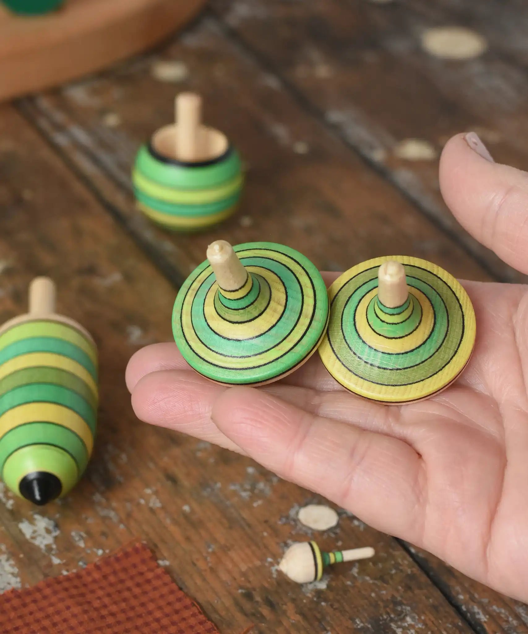 Two rallyes spinning tops from the Mader Kreiselmanufaktur green grass spinning top learning setin an adult's hand in the Babipur playroom. 