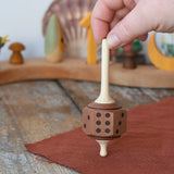 Mader Dice Spinning Top held upright by an adult's hand in the Babipur playroom.