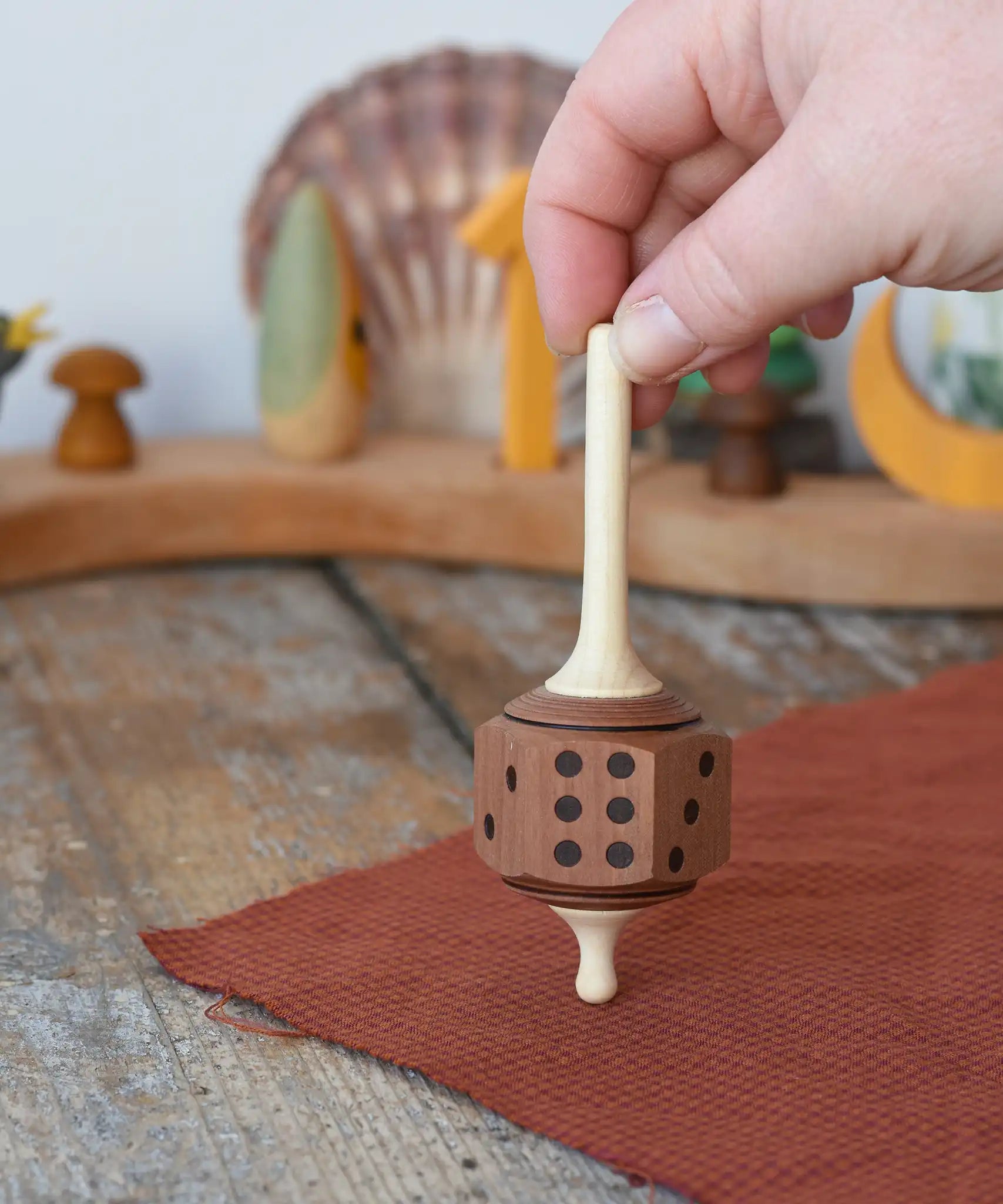 Mader Dice Spinning Top held upright by an adult's hand in the Babipur playroom.