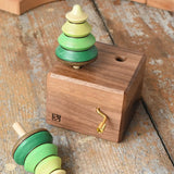 Mader Kreiselmanufaktur forest music box placed on a wooden desk in the Babipur playroom. A wooden wind up musical box with two slots for the green tree shaped spinners on the top. One tree has been taken out of the box.