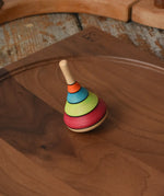Mader harlekin spinning top placed on a walnut wood plate on a wooden surface in the Babipur playroom.