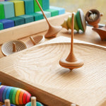 Mader wooden Ibis spinning top on a Mader spinning plate surrounded by wooden spinning tops and a Grimms Large Stepped Pyramid