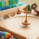 Mader wooden Ibis spinning top on a Mader spinning plate surrounded by wooden spinning tops and a Grimms Large Stepped Pyramid