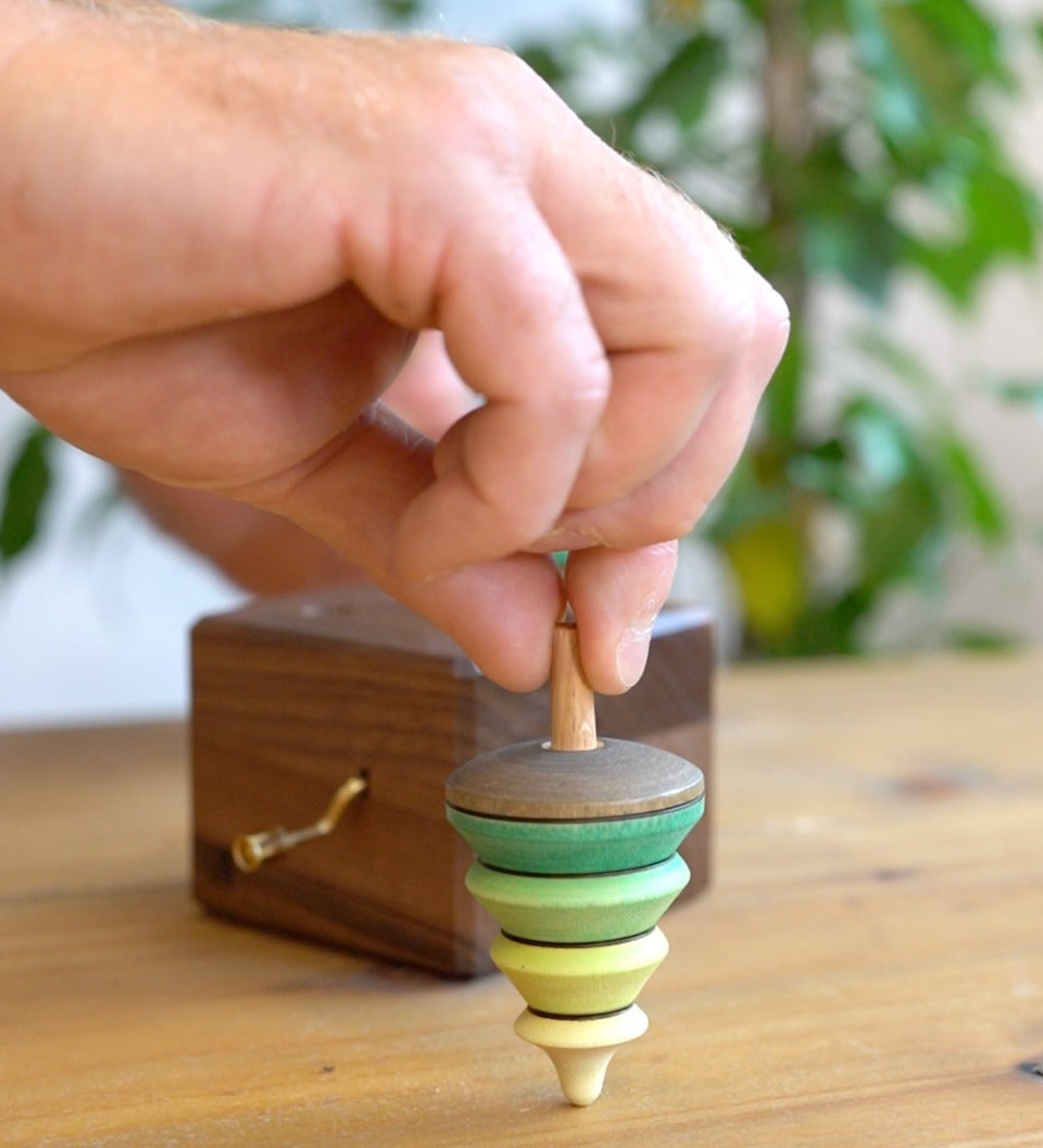 Close up of a hand holding the spinning top from the Mader wooden music box on a wooden table