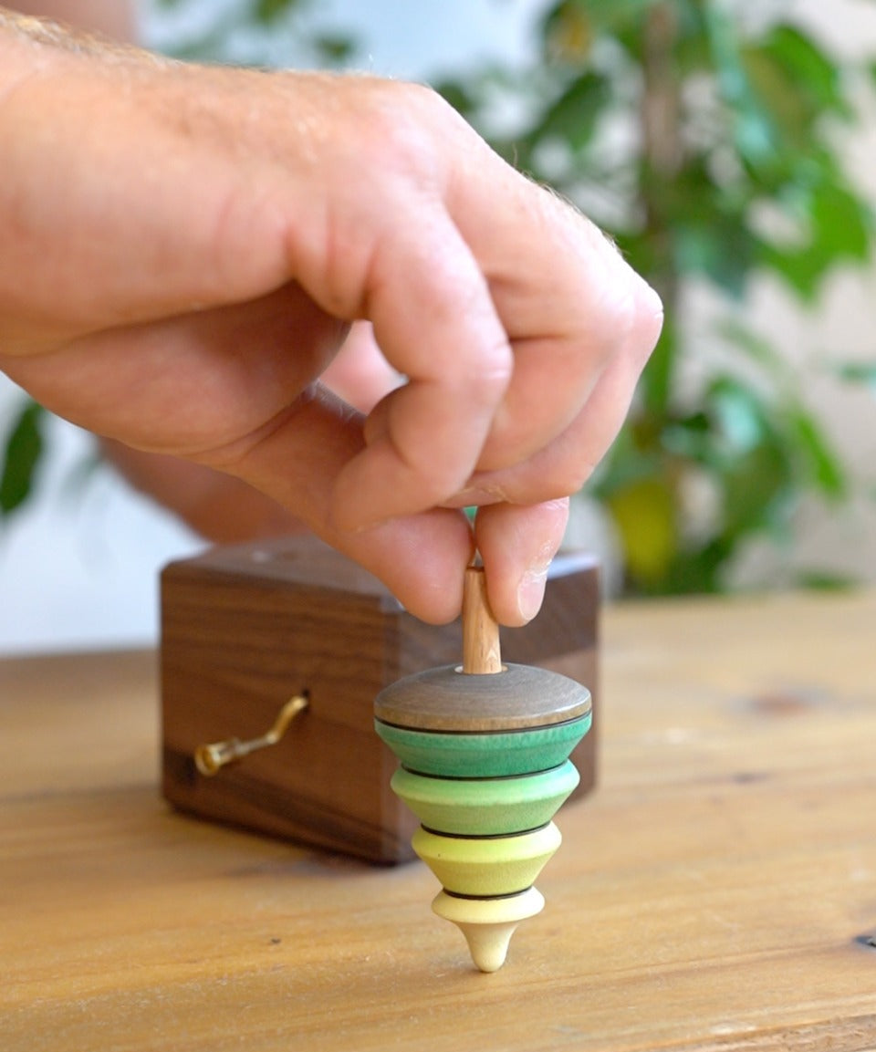Close up of a hand holding the spinning top from the Mader wooden music box on a wooden table