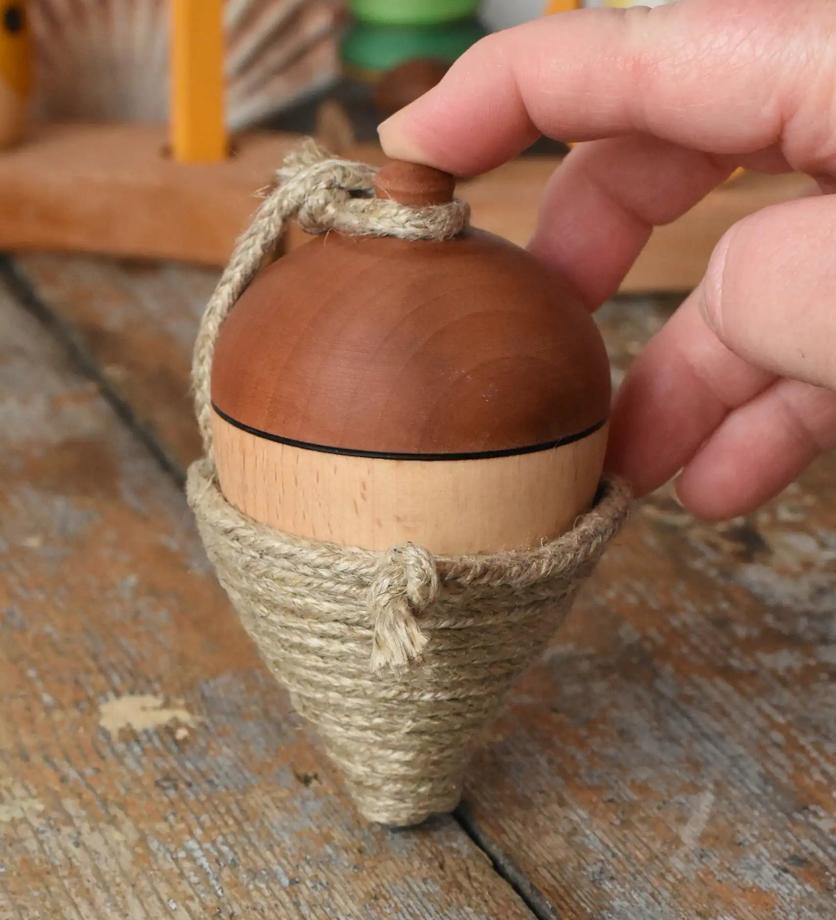 Mader natural profi throw spinning top placed on a wooden surface in the Babipur playroom. An adult hand propping it upright.