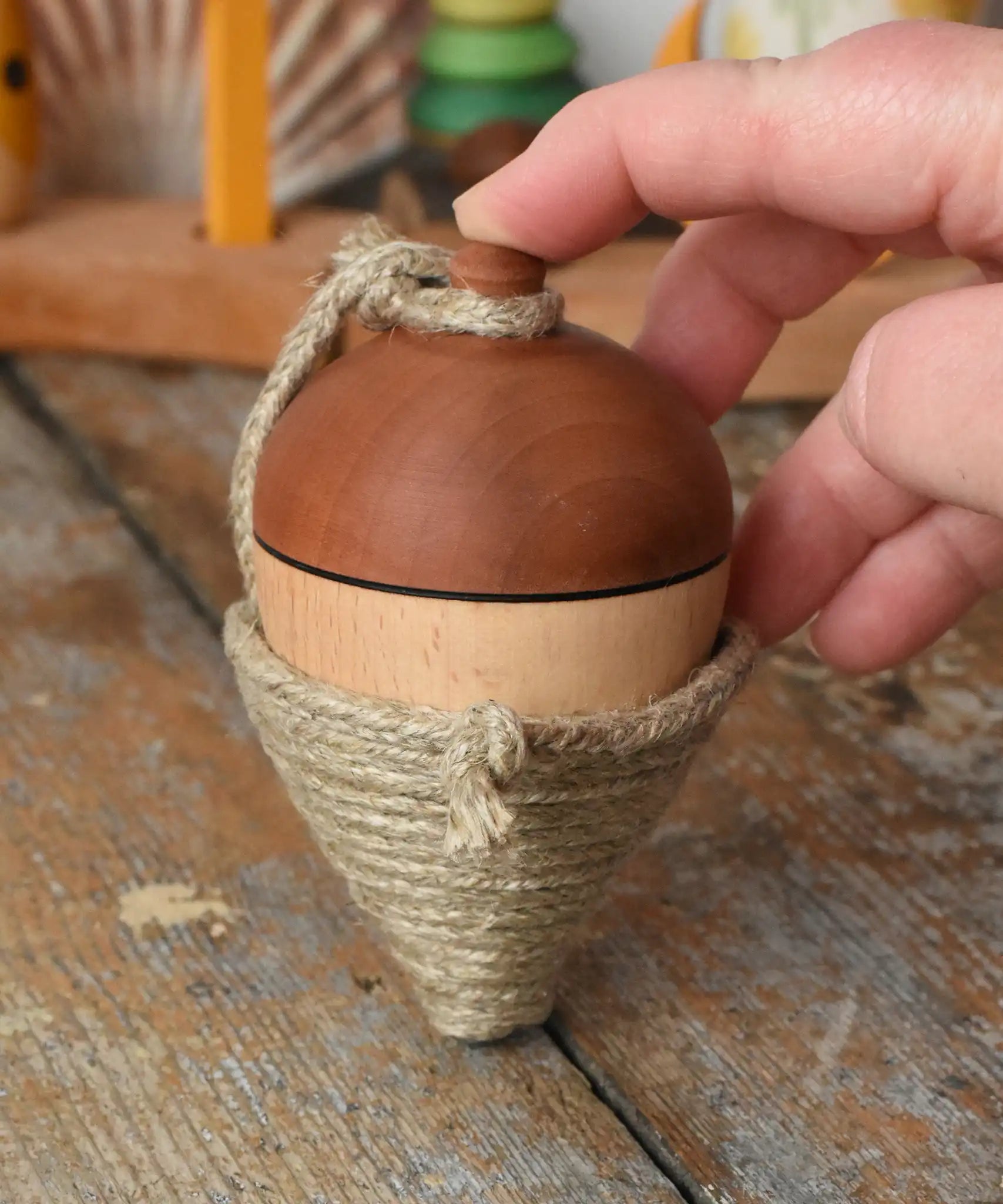 Mader natural profi throw spinning top placed on a wooden surface in the Babipur playroom. An adult hand propping it upright.