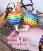 Two Mader Kreiselmanufaktur rainbow lolly spinning tops in an adult's hand.