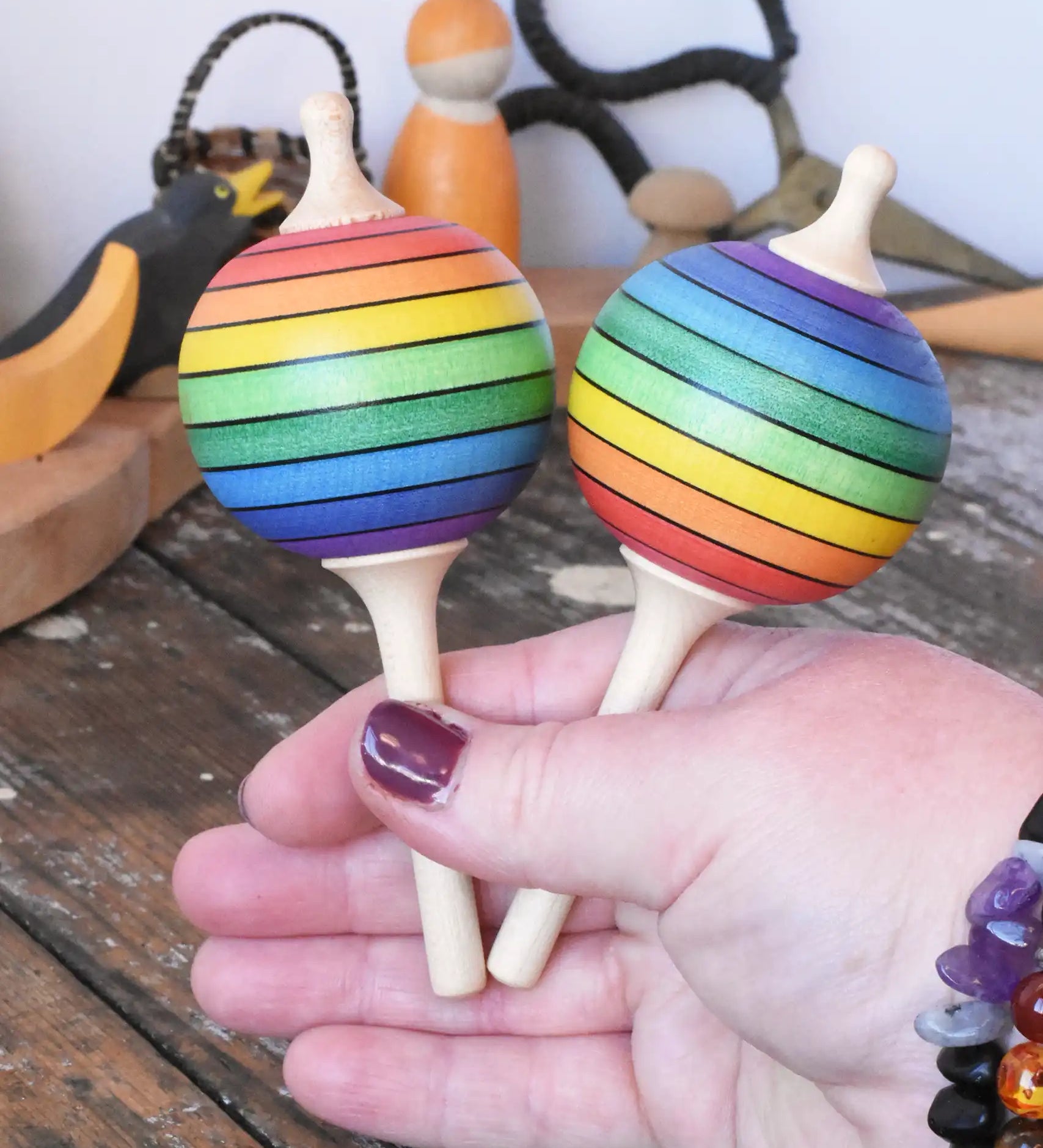 Two Mader Kreiselmanufaktur rainbow lolly spinning tops in an adult's hand.