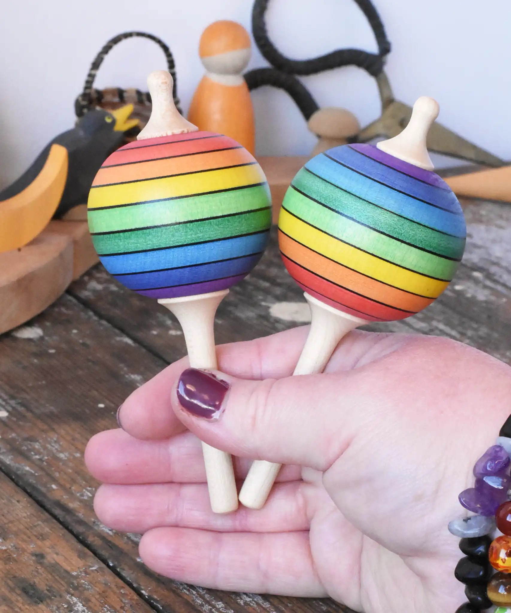 Two Mader Kreiselmanufaktur rainbow lolly spinning tops in an adult's hand.