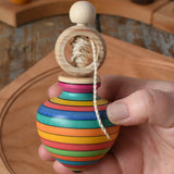 Mader Kreiselmanufaktur ring pull string spinning top in an adult's hand with a cherry wood spinning plate in the background in the Babipur playroom.