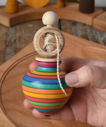 Mader Kreiselmanufaktur ring pull string spinning top in an adult's hand with a cherry wood spinning plate in the background in the Babipur playroom.