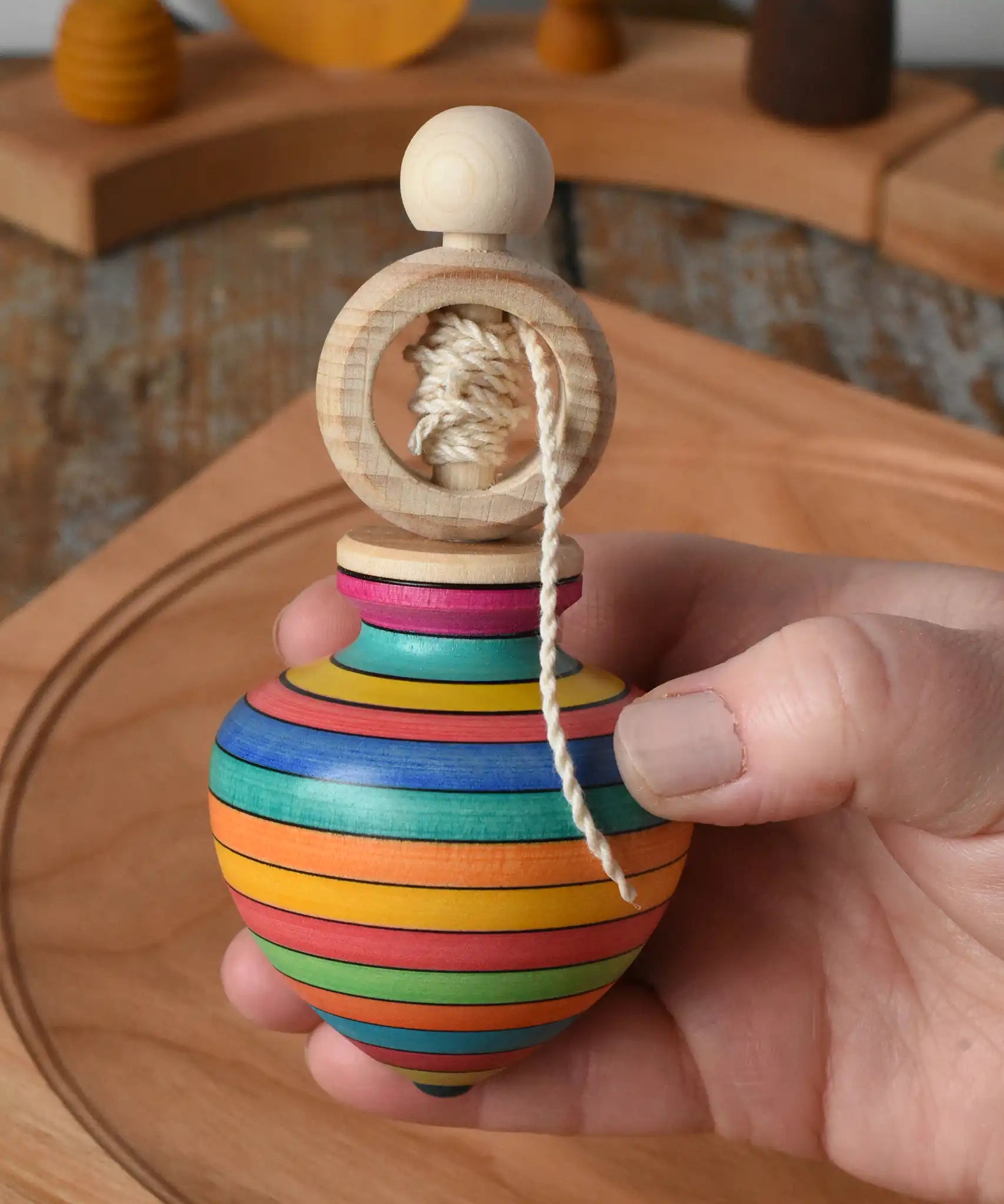 Mader Kreiselmanufaktur ring pull string spinning top in an adult's hand with a cherry wood spinning plate in the background in the Babipur playroom.