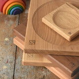 Close up of a stack of handmade Mader spinning plates in different woods, cherry, ash, walnut and oak placed on a wooden surface in the Babipur playroom. 