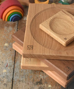 Close up of a stack of handmade Mader spinning plates in different woods, cherry, ash, walnut and oak placed on a wooden surface in the Babipur playroom. 