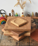 A stack of handmade Mader spinning plates in different woods, cherry, ash, walnut and oak placed on a wooden surface in the Babipur playroom. 