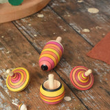 Mader fire spinning top learning set placed on a wooden surface in the Babipur playroom. Mix of pink, orange and yellow shade stripes.