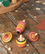 Mader fire spinning top learning set placed on a wooden surface in the Babipur playroom. Mix of pink, orange and yellow shade stripes.