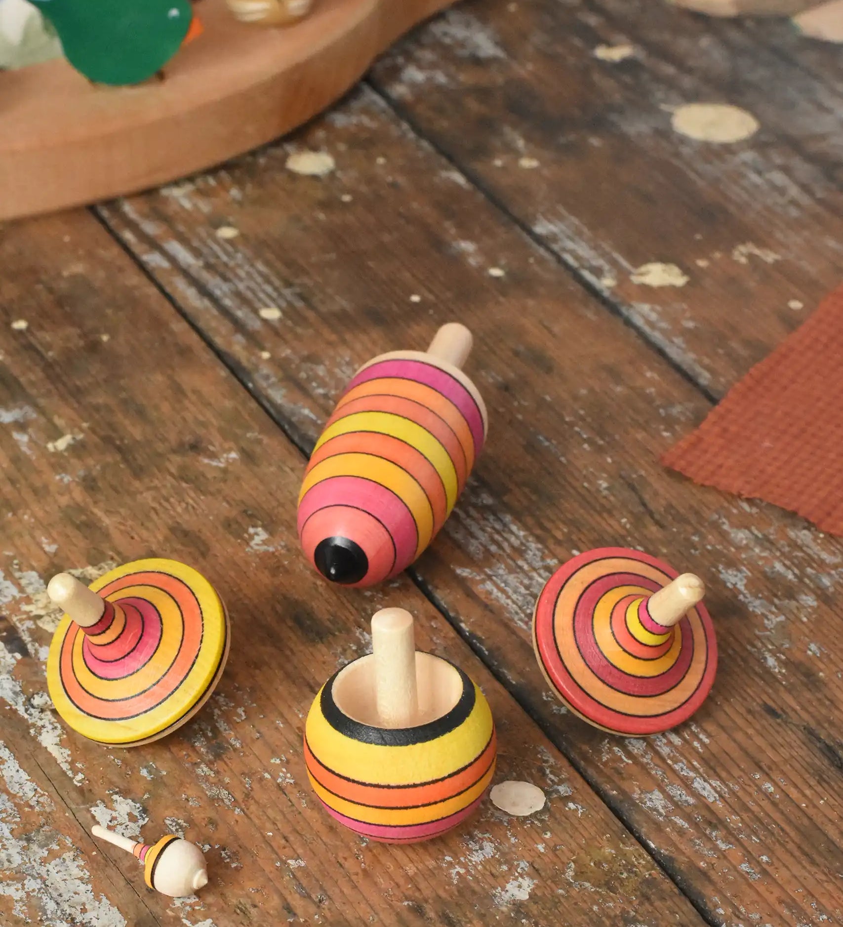 Mader fire spinning top learning set placed on a wooden surface in the Babipur playroom. Mix of pink, orange and yellow shade stripes.