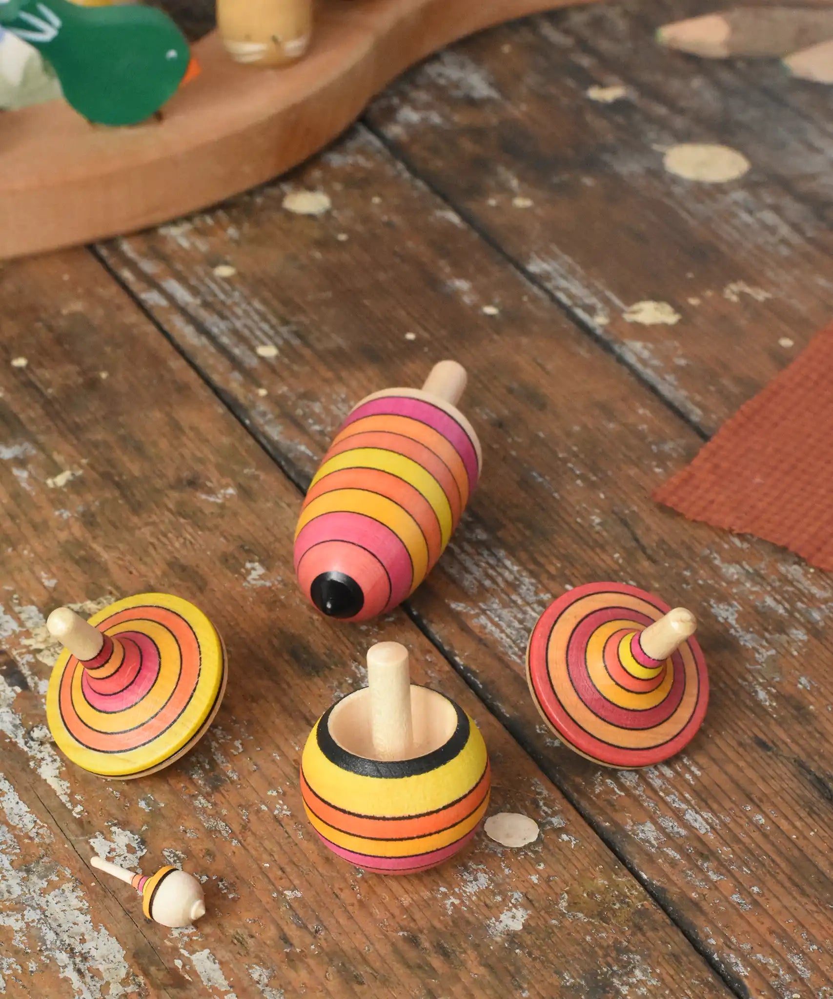Mader fire spinning top learning set placed on a wooden surface in the Babipur playroom. Mix of pink, orange and yellow shade stripes.