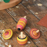 Mader fire spinning top learning set placed on a wooden surface in the Babipur playroom. Mix of pink, orange and yellow shade stripes.