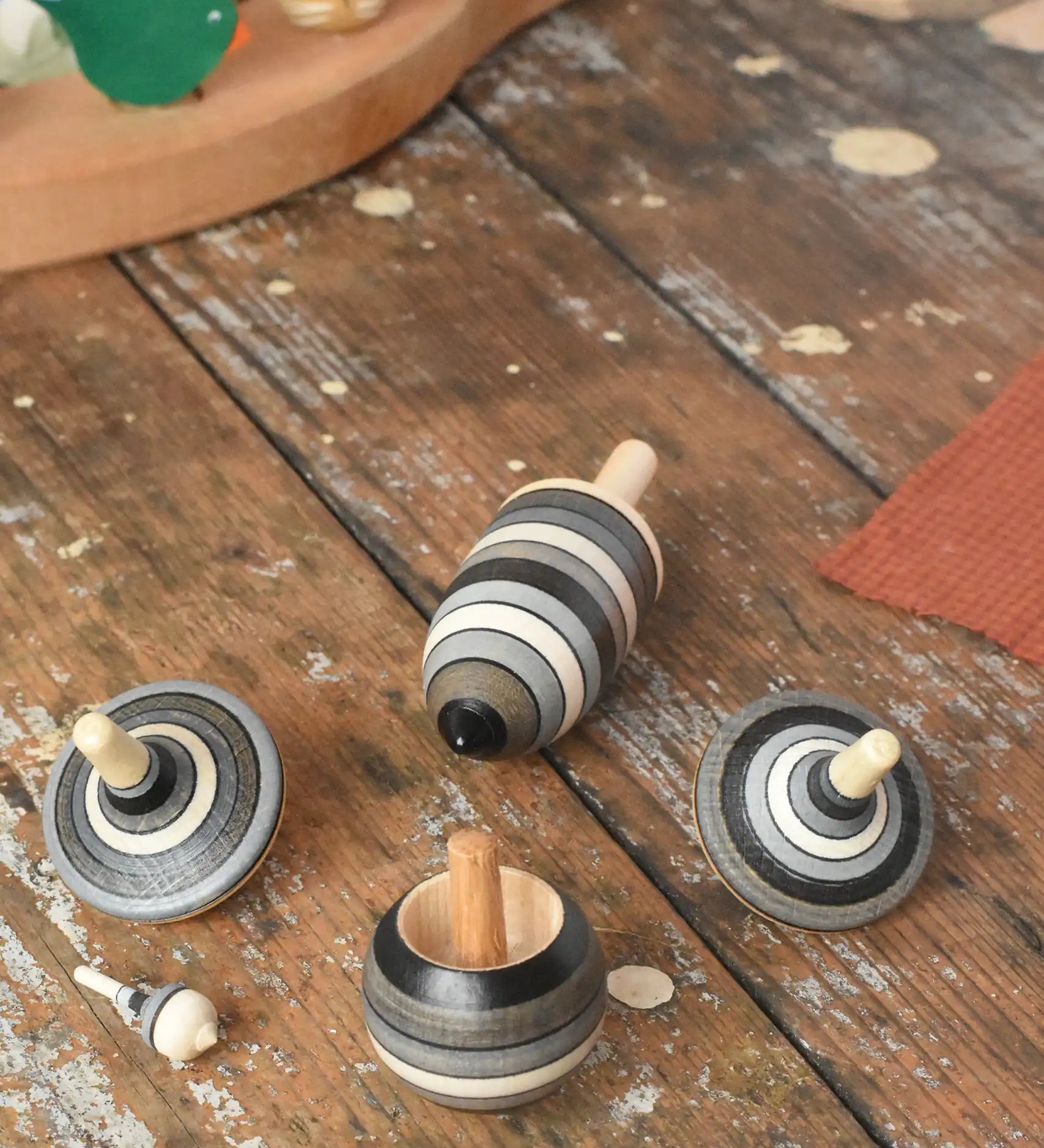 Mader Kreiselmanufaktur graphite spinning top learning set placed on a wooden surface in the Babipur playroom. The set has 5 striped tops in shades of grey, white and black.