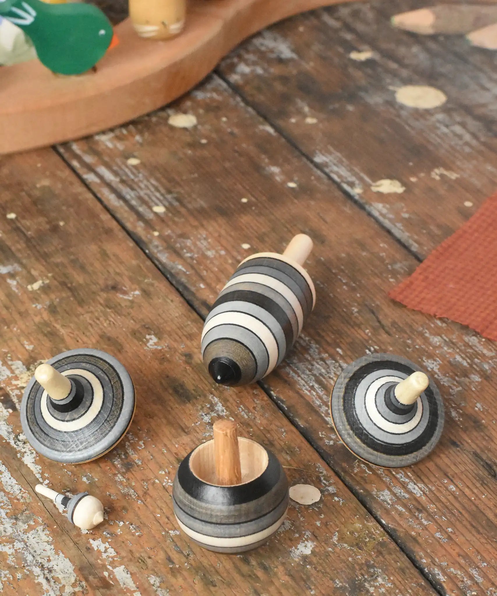 Mader Kreiselmanufaktur graphite spinning top learning set placed on a wooden surface in the Babipur playroom. The set has 5 striped tops in shades of grey, white and black.