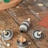 Mader Kreiselmanufaktur graphite spinning top learning set placed on a wooden surface in the Babipur playroom. The set has 5 striped tops in shades of grey, white and black.