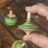 Rallye spinning top from the Mader Kreiselmanufaktur green grass spinning top learning set shown in an adult's hand in the Babipur playroom. 