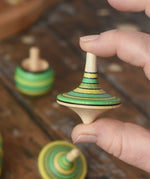 Rallye spinning top from the Mader Kreiselmanufaktur green grass spinning top learning set shown in an adult's hand in the Babipur playroom. 