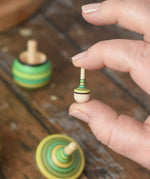 Miniature spinner from the Mader Kreiselmanufaktur green grass spinning top learning set in an adult's hand in the Babipur playroom. 