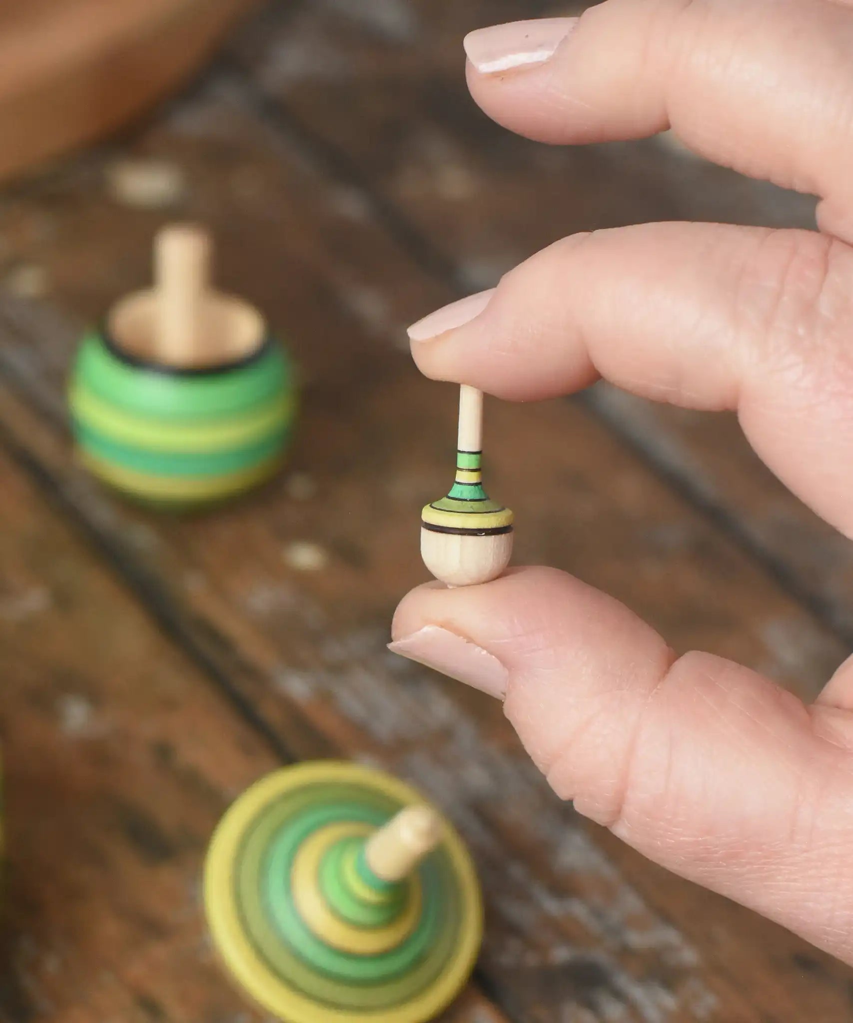 Miniature spinner from the Mader Kreiselmanufaktur green grass spinning top learning set in an adult's hand in the Babipur playroom. 