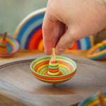 Close up of a hand holding a mader plastic free wooden sombrero spinning top on a mader spinning plate