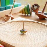 Close up of the Mader mini superstar spinning top on a Mader spinning plate next to some wooden spinning tops