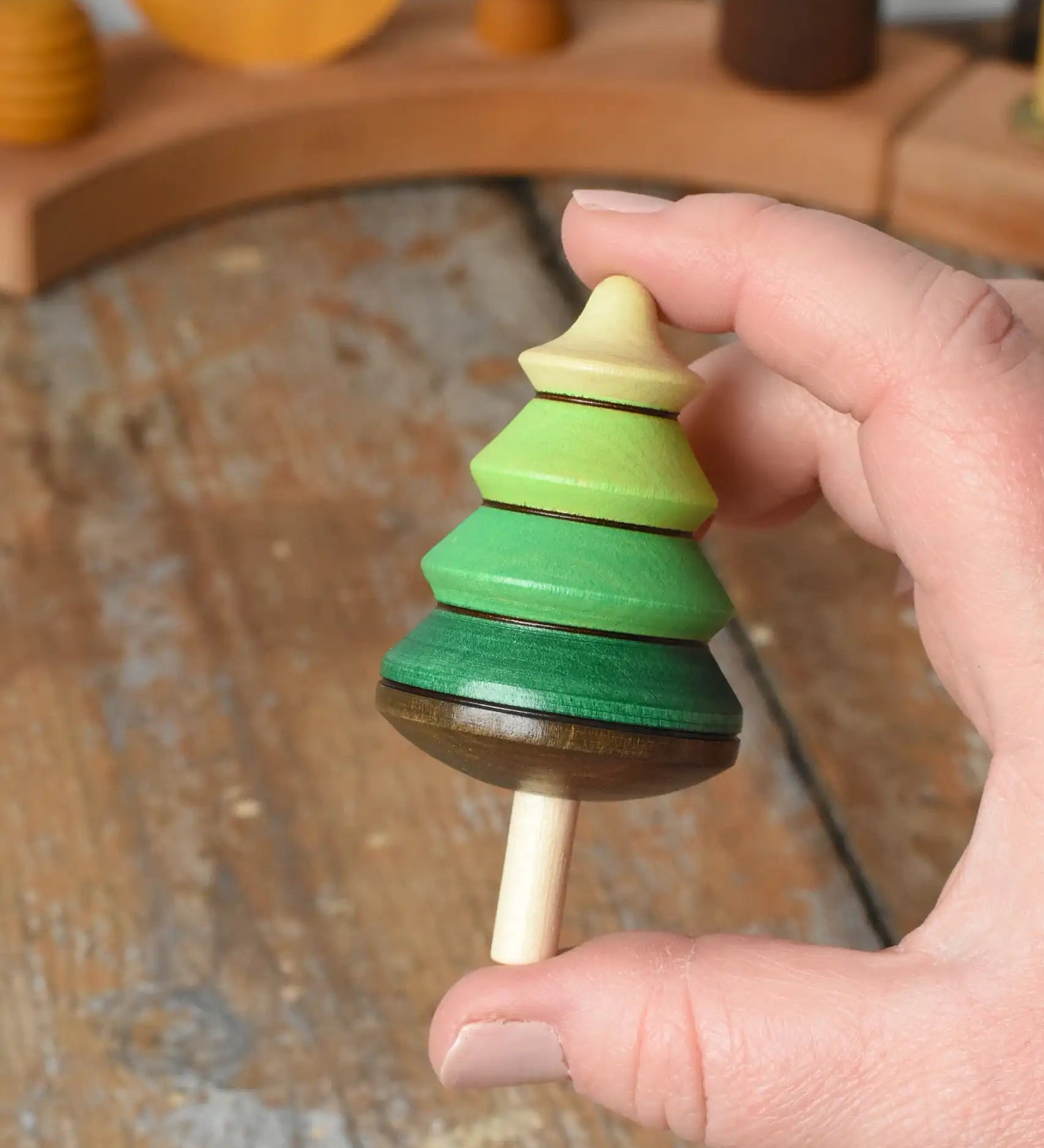 Mader Kreiselmanufaktur green tree spinning top in an adult's hand in the Babipur playroom.