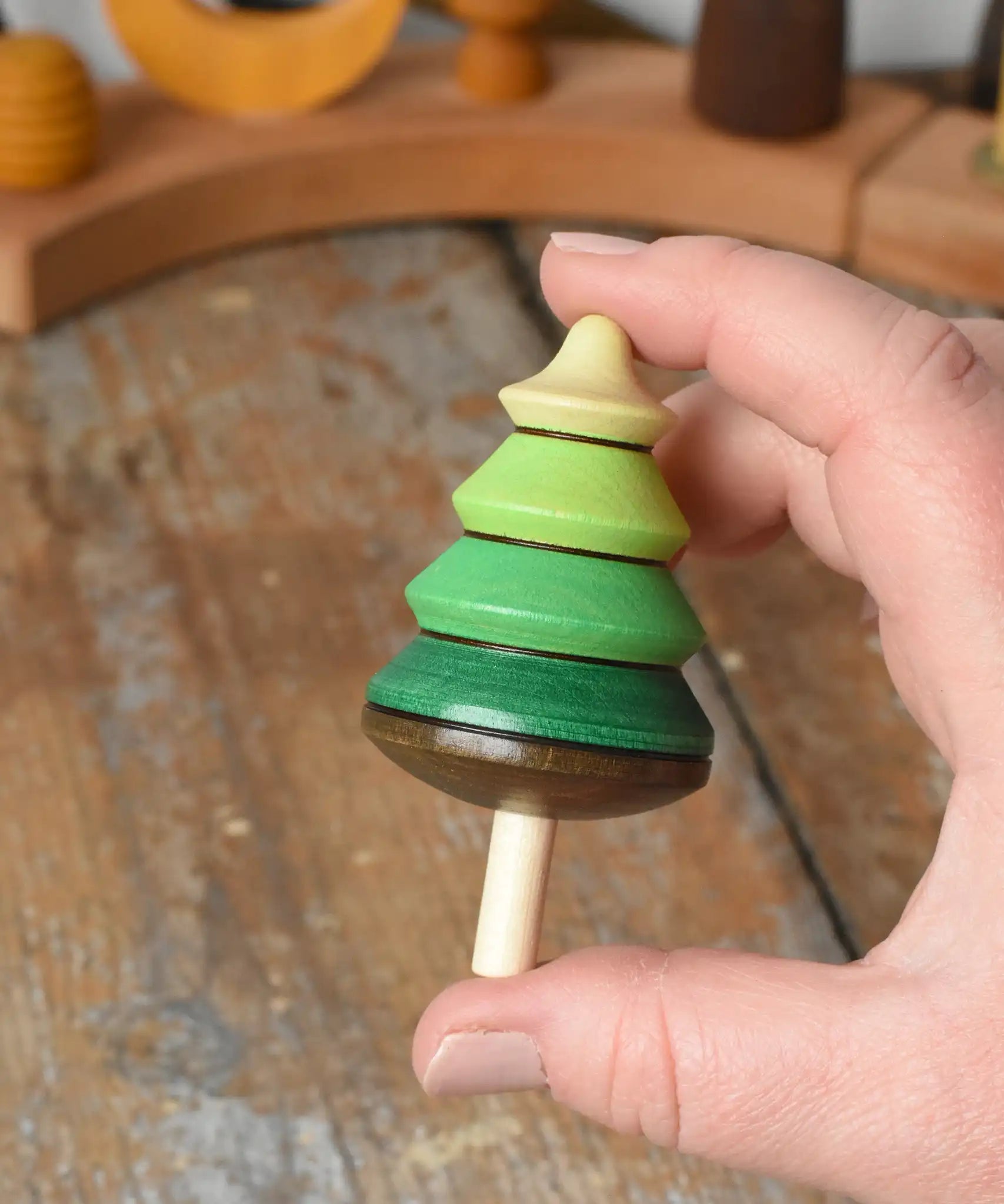 Mader Kreiselmanufaktur green tree spinning top in an adult's hand in the Babipur playroom.